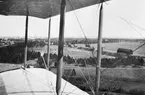 Flygfotografi genom vinge på flygplan Albatros vid landning på Flygkompaniet på Malmen, omkring 1920-1925. Till vänster syns I 4 och I 5 lägerområde med Röda och Gula förråden, till höger landsvägen mot Malmslätt.