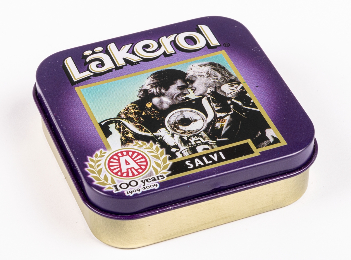 Tablettask i plåt för Läkerol. Lila färg med svartvit bild av par på motorcykel. Text "Läkerol SALVI 100 years 1909 - 2009". Innehållsförteckning på undersidan.