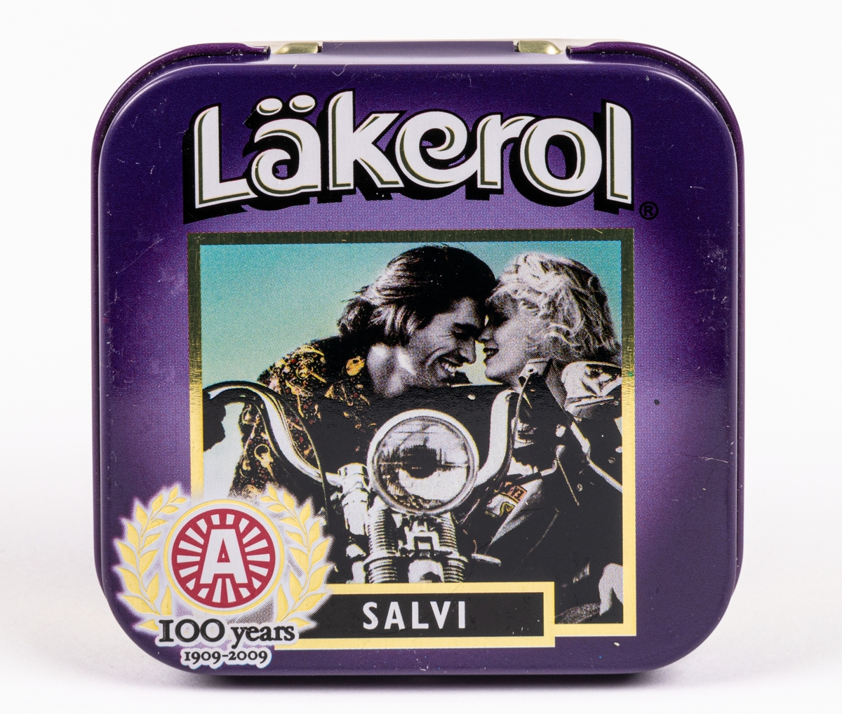 Tablettask i plåt för Läkerol. Lila färg med svartvit bild av par på motorcykel. Text "Läkerol SALVI 100 years 1909 - 2009". Innehållsförteckning på undersidan.