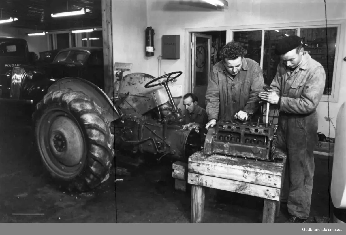 Frå Fylkesyrkesskulen på Dovre. Arbeid med ein motor det andre året med ordinær opplæring i landbruksmekanikk. Bak traktoren sit lærar Jakob Sagflaten på huk.