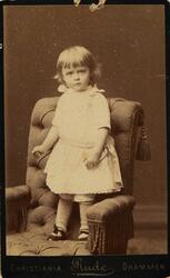 Portrett av liten jente stående i en stol.