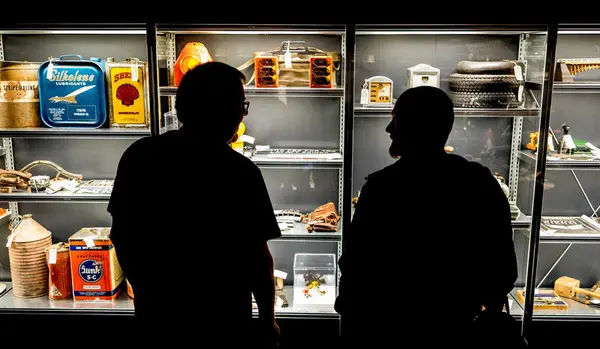 Silhuett av to besøkende foran et glassmonter med gjenstander på utstillingen Drift