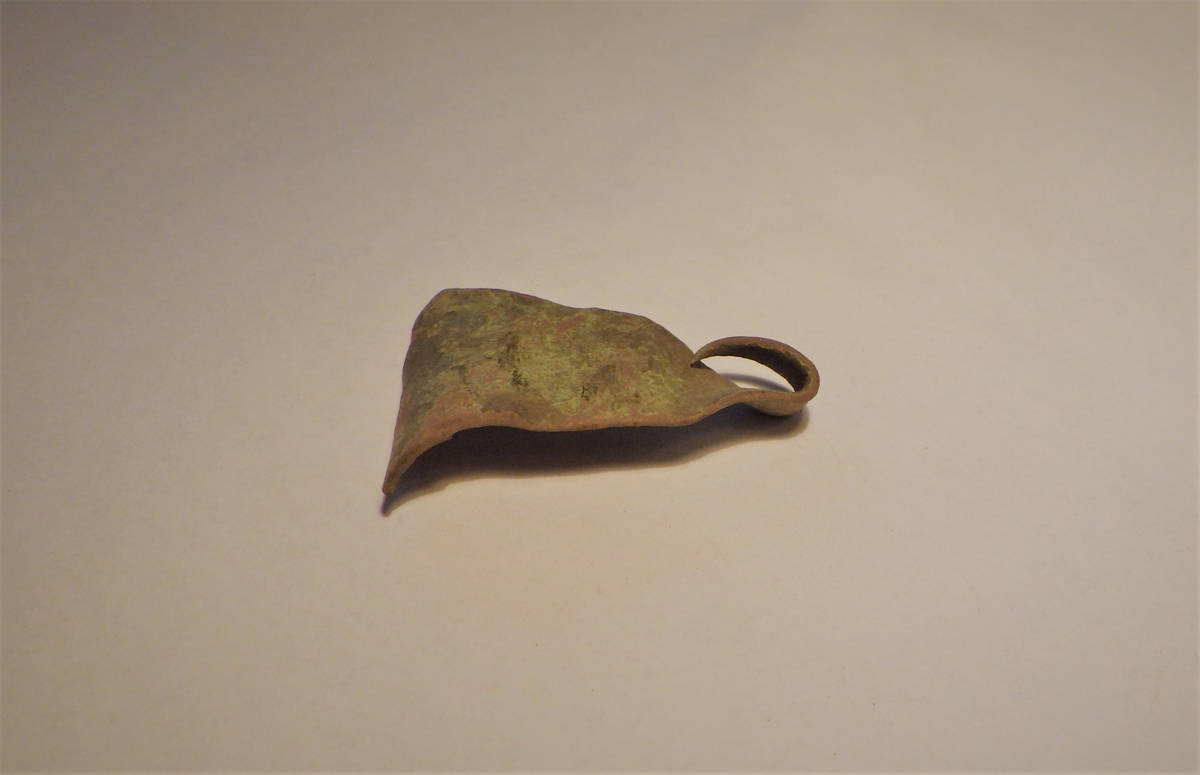 TYnn og jevn metallplate med trekantform. En av spissene er brettet inn. Gjenstanden er et halvfabrikat til en nagle. 