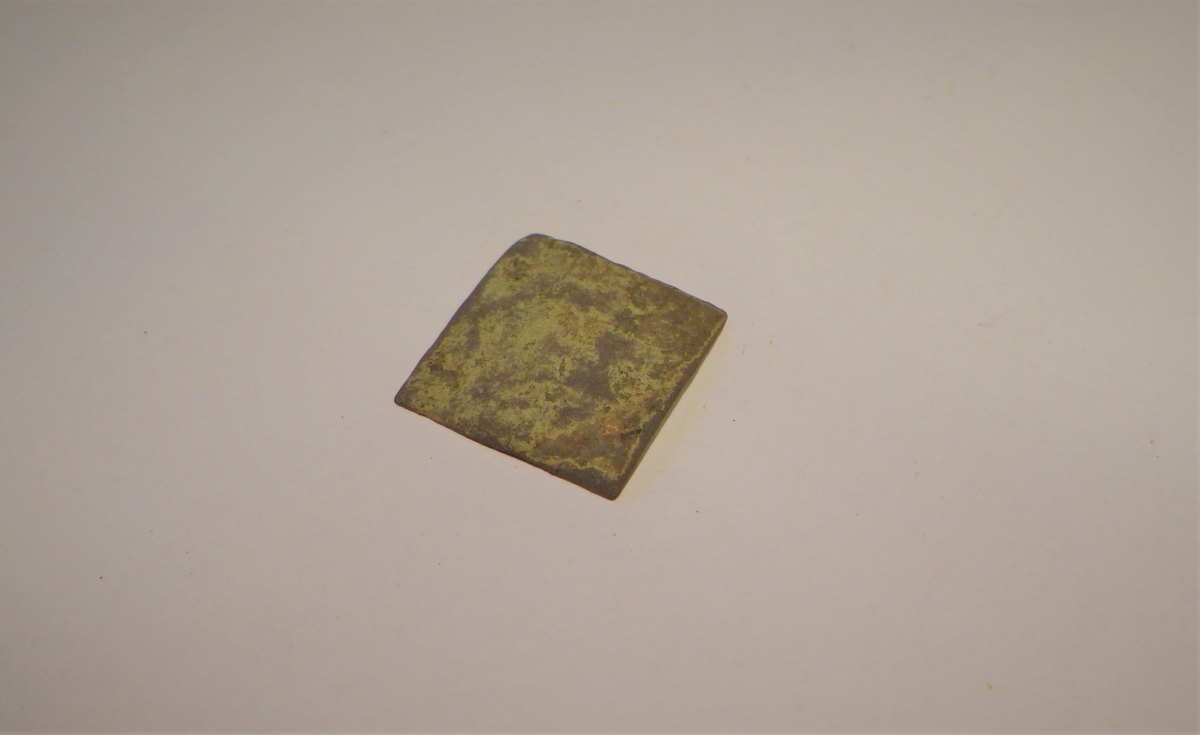 Tilnærmet kvadratisk metallplate som kan være et halvfabrikat til en kobbernagle.