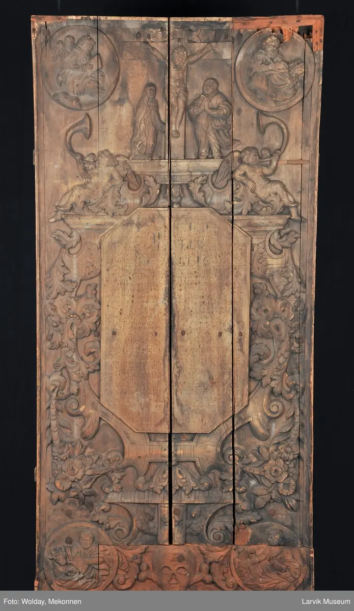 Midtfeltet for påsetting av skrift, omgitt av korsfestelsen, engler, dødssymboler og akantusløv. I hjørnene medaljonger med bilder av de fire evangelister