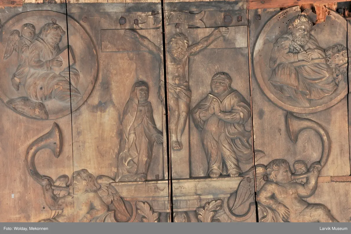 Midtfeltet for påsetting av skrift, omgitt av korsfestelsen, engler, dødssymboler og akantusløv. I hjørnene medaljonger med bilder av de fire evangelister