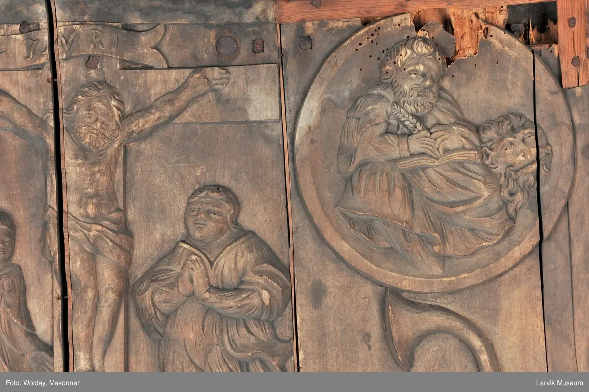 Midtfeltet for påsetting av skrift, omgitt av korsfestelsen, engler, dødssymboler og akantusløv. I hjørnene medaljonger med bilder av de fire evangelister