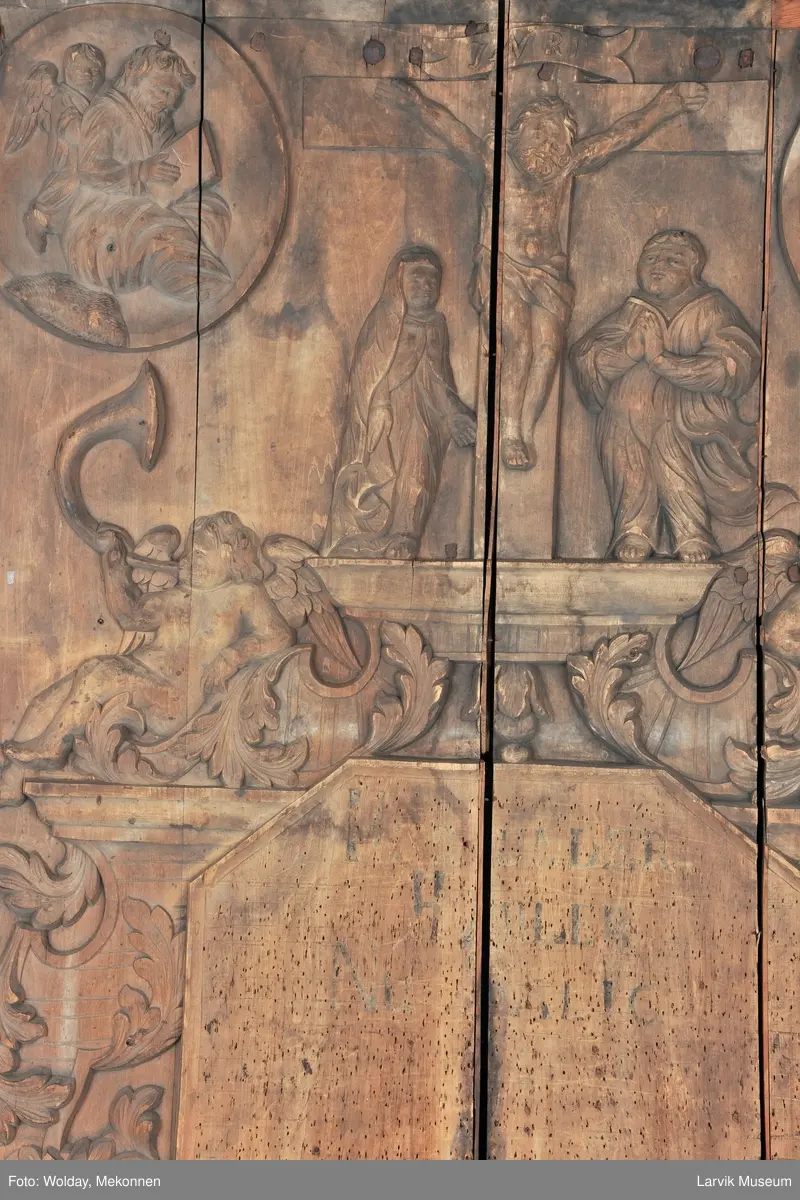 Midtfeltet for påsetting av skrift, omgitt av korsfestelsen, engler, dødssymboler og akantusløv. I hjørnene medaljonger med bilder av de fire evangelister