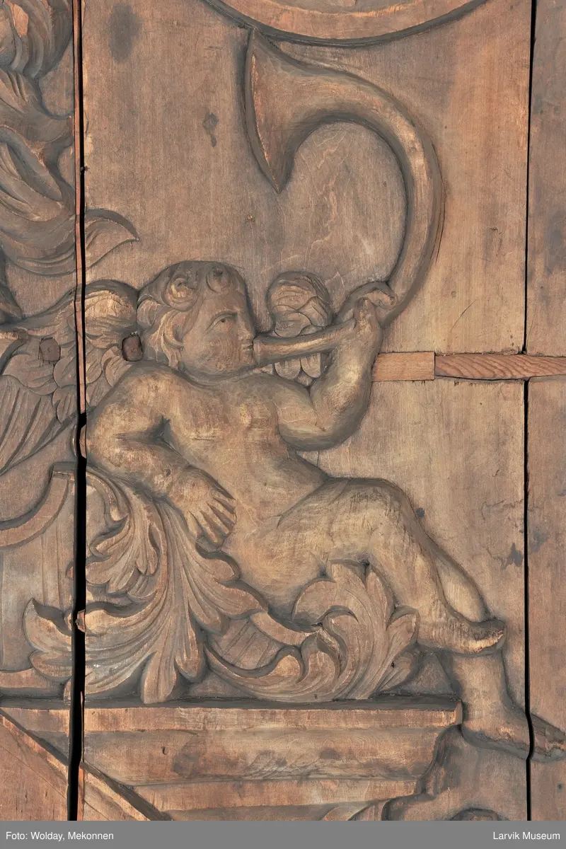 Midtfeltet for påsetting av skrift, omgitt av korsfestelsen, engler, dødssymboler og akantusløv. I hjørnene medaljonger med bilder av de fire evangelister