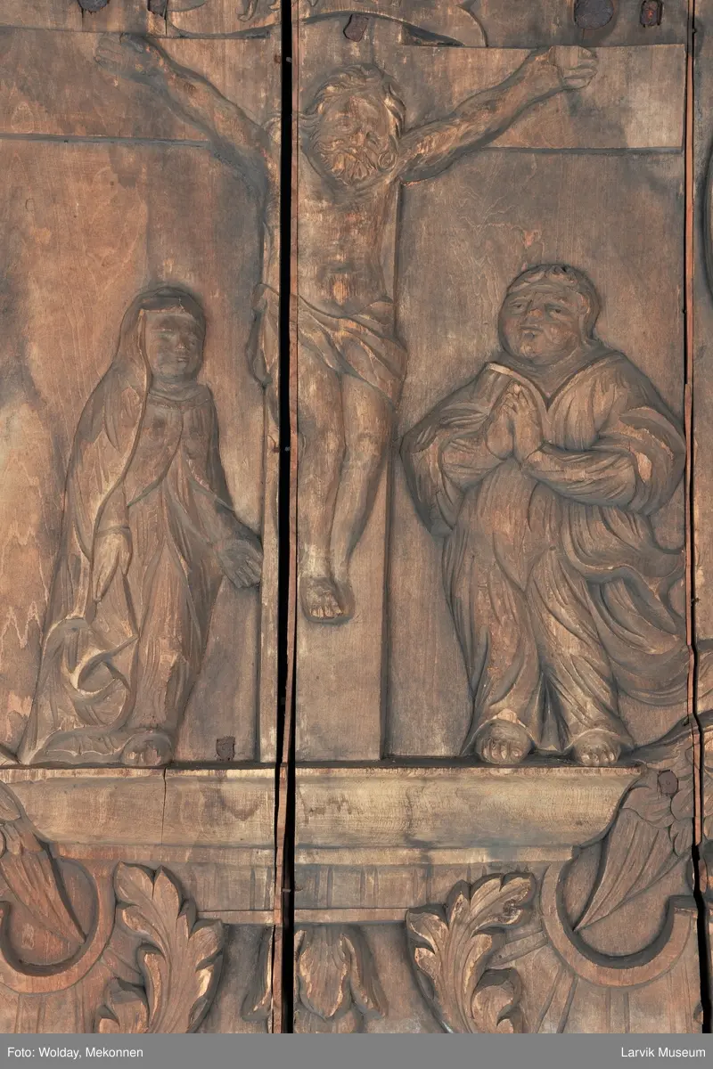 Midtfeltet for påsetting av skrift, omgitt av korsfestelsen, engler, dødssymboler og akantusløv. I hjørnene medaljonger med bilder av de fire evangelister