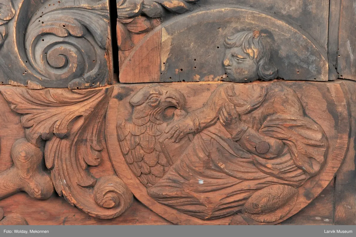 Midtfeltet for påsetting av skrift, omgitt av korsfestelsen, engler, dødssymboler og akantusløv. I hjørnene medaljonger med bilder av de fire evangelister