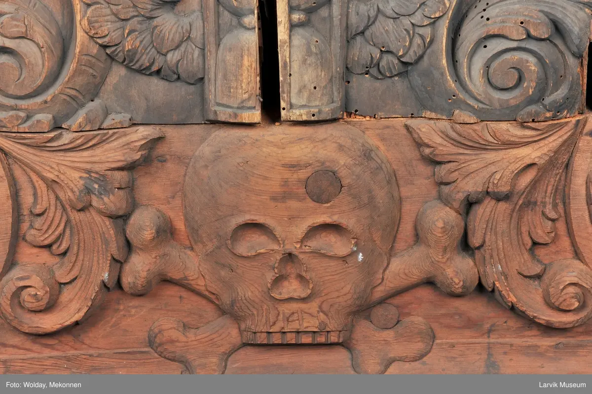 Midtfeltet for påsetting av skrift, omgitt av korsfestelsen, engler, dødssymboler og akantusløv. I hjørnene medaljonger med bilder av de fire evangelister