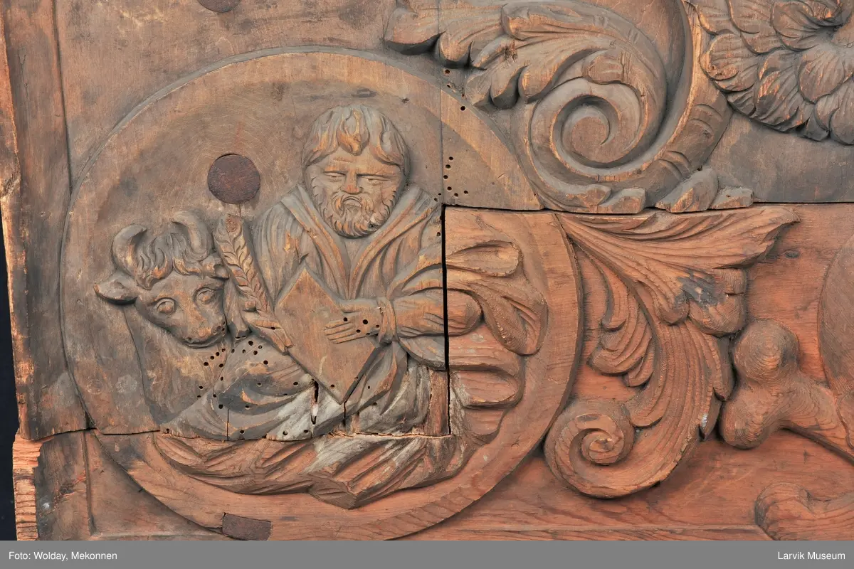 Midtfeltet for påsetting av skrift, omgitt av korsfestelsen, engler, dødssymboler og akantusløv. I hjørnene medaljonger med bilder av de fire evangelister