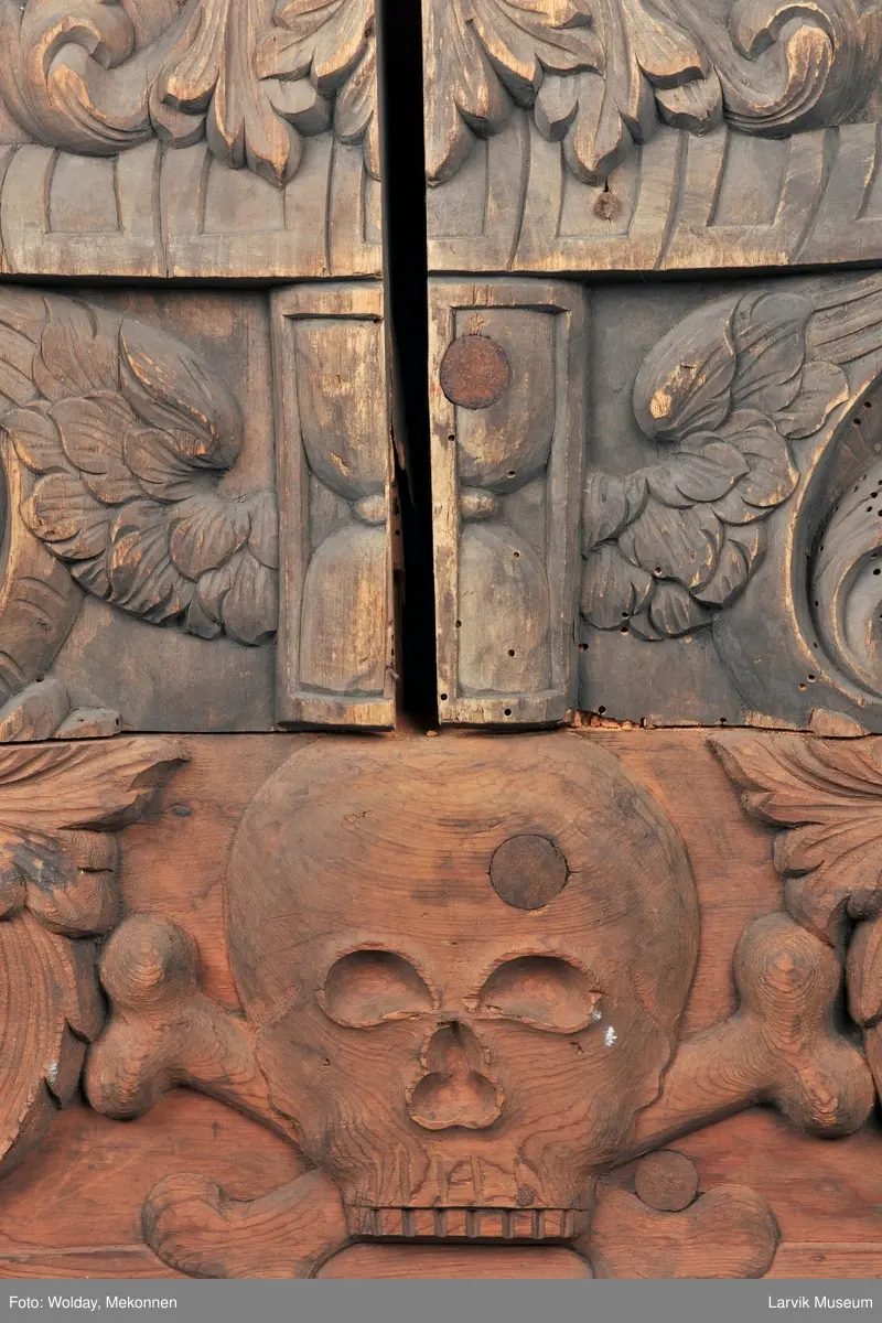 Midtfeltet for påsetting av skrift, omgitt av korsfestelsen, engler, dødssymboler og akantusløv. I hjørnene medaljonger med bilder av de fire evangelister