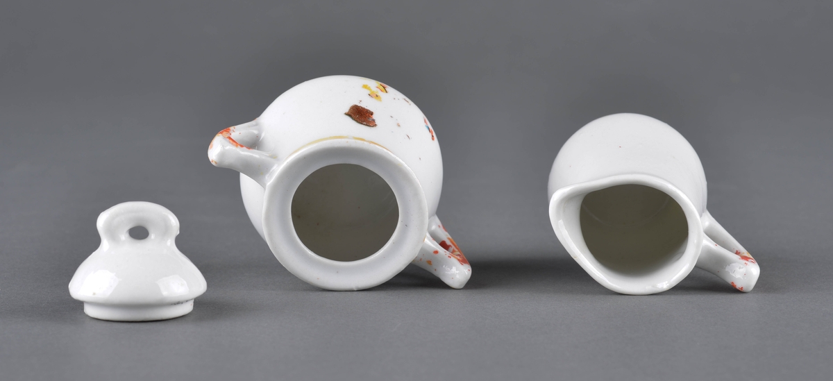 Sett med fløtemugge og sukkerskål.
Muggen har hanke med delvis avslitt rød dekor og et dekorbilde på ene siden, som er delvis slitt av. 
Sukkerskåla har håndtak på hver side og et lokk. Rød dekorlinje rundt åpningen på på hankene, som er delvis slitt av. 
Sukkerskåla har også dekorbilde på siden, som er nesten slitt av.