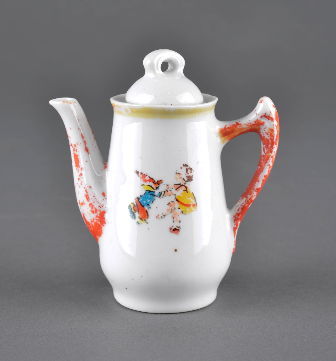 Te- eller kaffekanne med lokk
Kannen har tut og hanke med delvis avslitt rød dekor og et dekorbilde på ene siden, som er delvis slitt av.