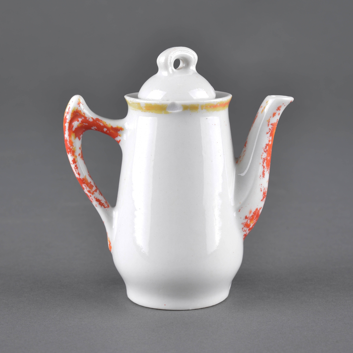 Te- eller kaffekanne med lokk
Kannen har tut og hanke med delvis avslitt rød dekor og et dekorbilde på ene siden, som er delvis slitt av.