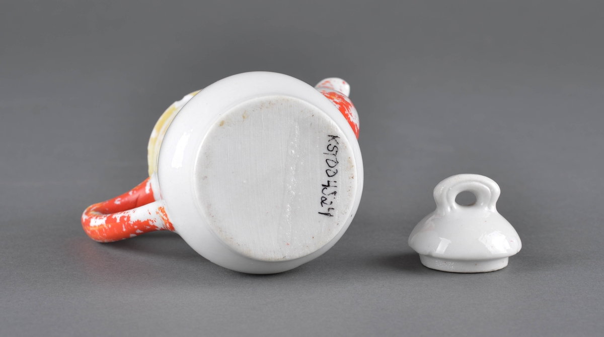 Te- eller kaffekanne med lokk
Kannen har tut og hanke med delvis avslitt rød dekor og et dekorbilde på ene siden, som er delvis slitt av.