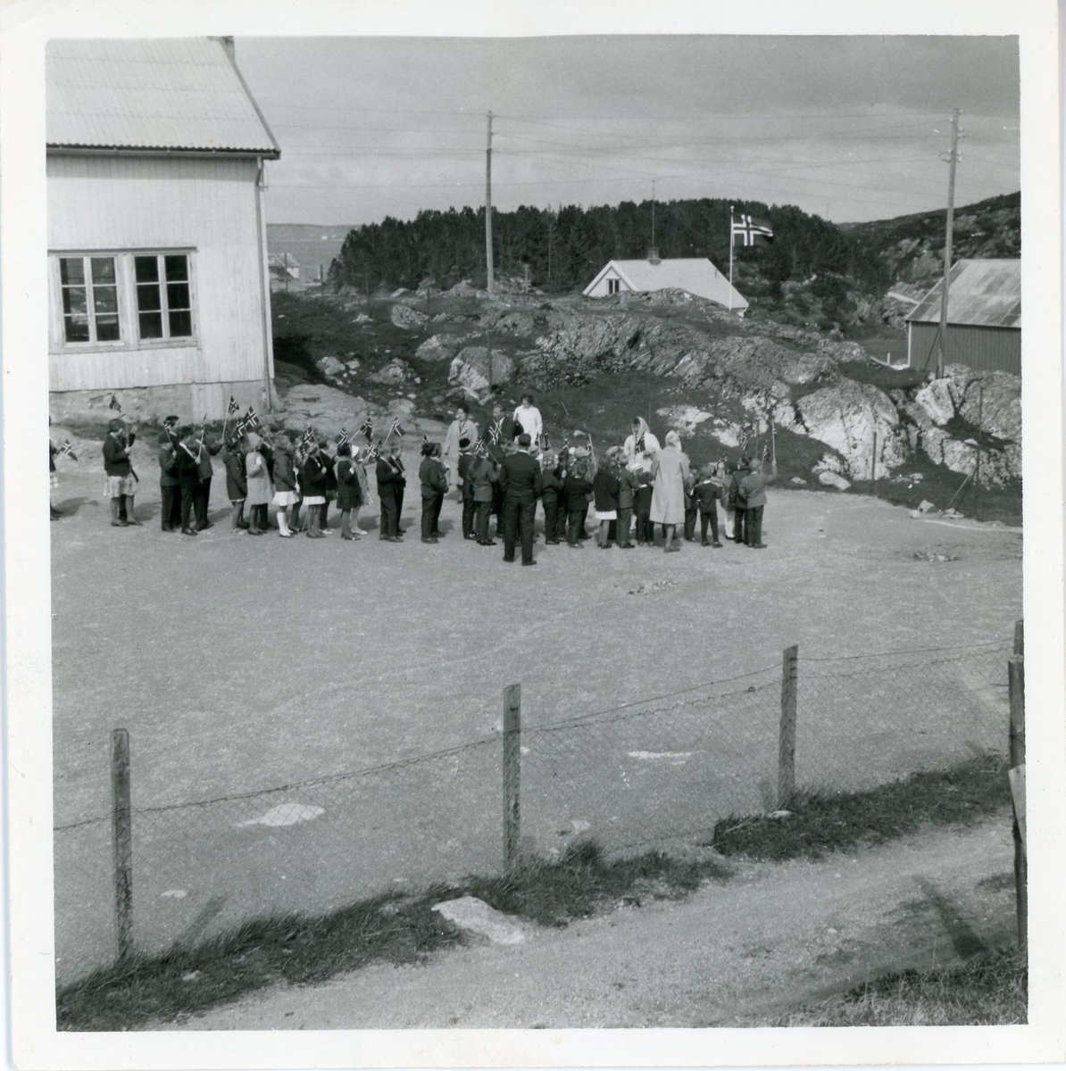 Barnetog utenfor en skole, bebyggelse og landskap i bakgrunnen.