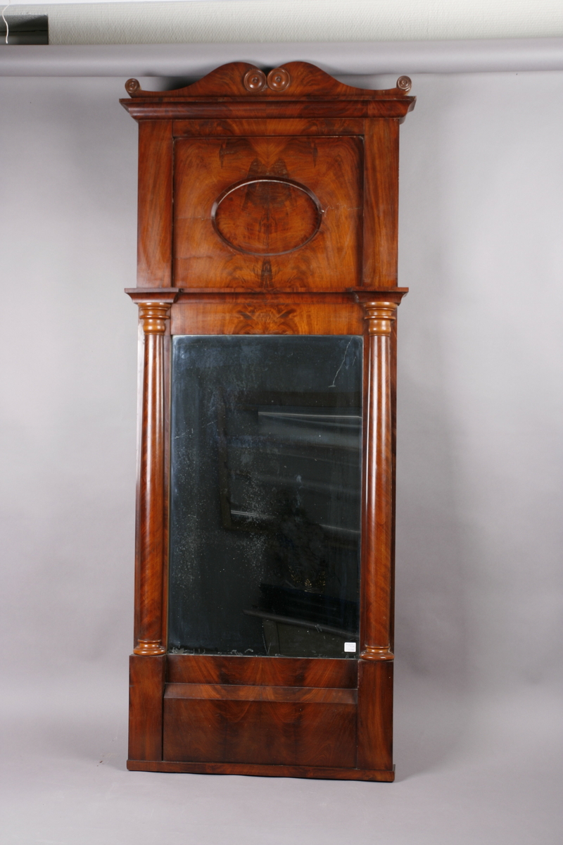 Biedermeier speil i treramme. Innfelt oval dekor på feltet på toppen. Øverst skåret dekor med sirkler. Søyler på hver side av speilet. Mahogny? Polert.