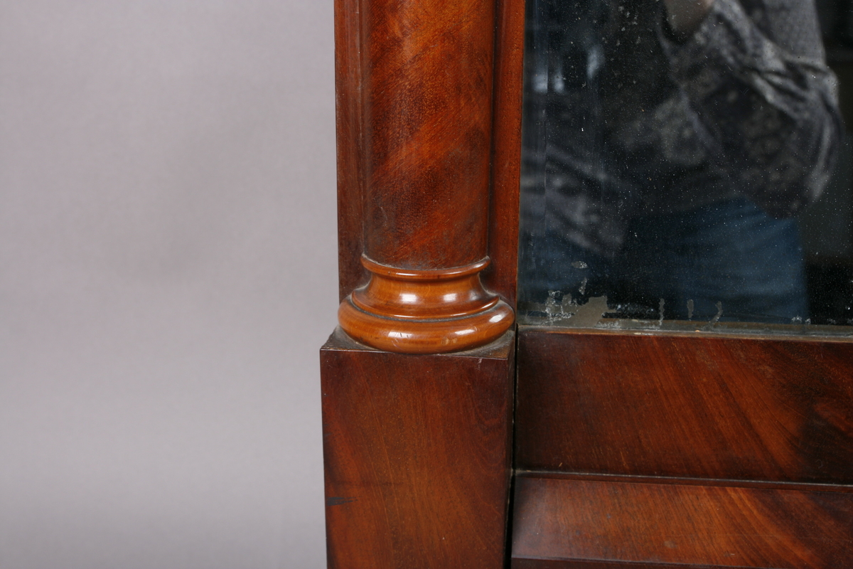Biedermeier speil i treramme. Innfelt oval dekor på feltet på toppen. Øverst skåret dekor med sirkler. Søyler på hver side av speilet. Mahogny? Polert.