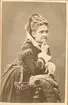 Kabinettsfotografi av en kvinna. Hon står lutad mot en stolsrygg.