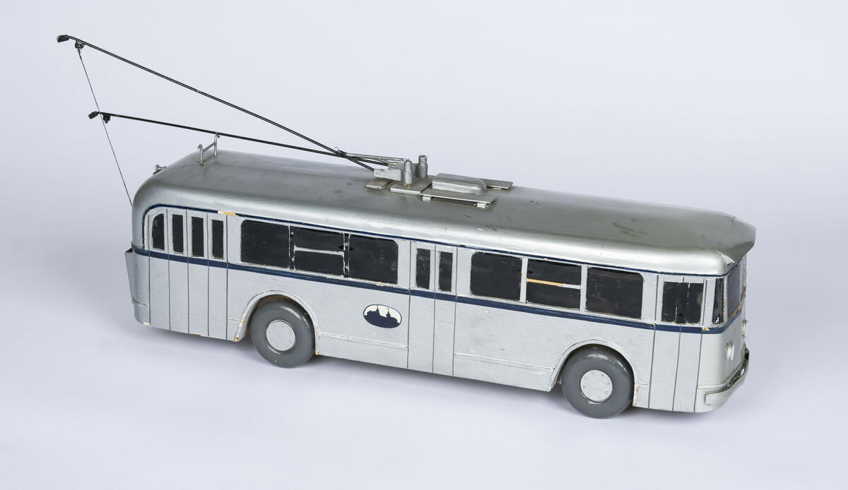 Modell av tre av buss A-1577. Bussen er farget i en sølvfarge med en mørk blå stripe på midten som går rundt hele modellen. Vinduene er farget sorte og de fire dekkene av tre er i en mørk grå farge. Bussen har tre inngangs- og utgangsdører. Denne modellen har to trolleystenger med kontakssko på enden og to trolleystenger som er festet til to snorspoler på baken av bussen. På enden av taket er det også plassert kroker for å feste trolleystengene når når ikker er i bruk.