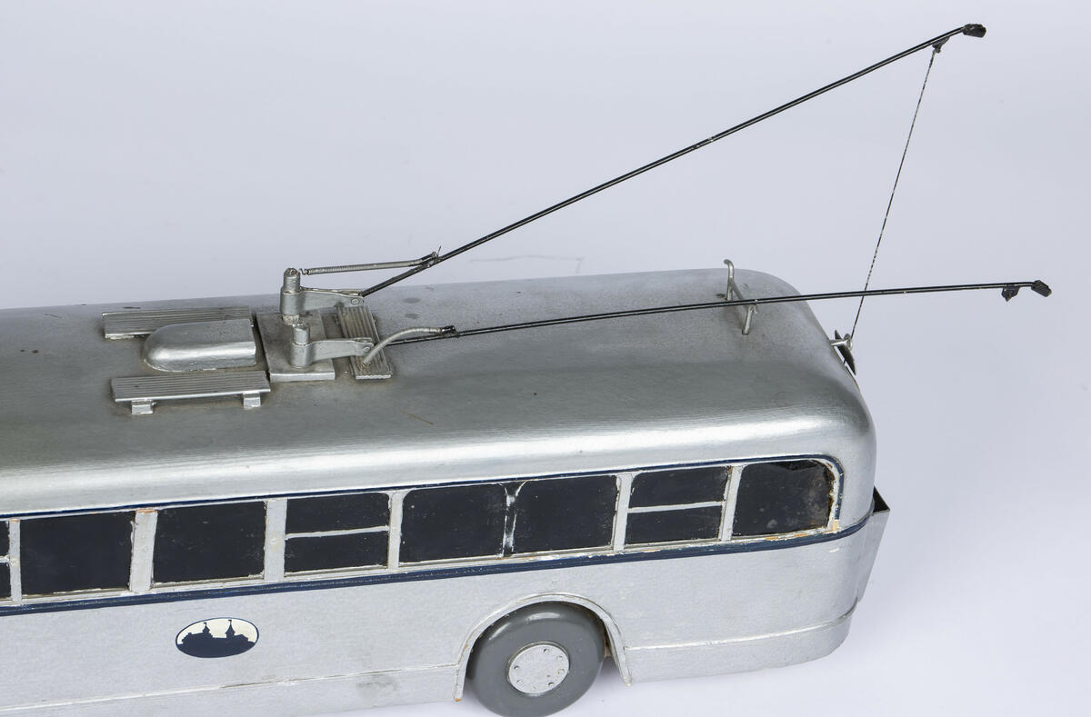 Modell av tre av buss A-1577. Bussen er farget i en sølvfarge med en mørk blå stripe på midten som går rundt hele modellen. Vinduene er farget sorte og de fire dekkene av tre er i en mørk grå farge. Bussen har tre inngangs- og utgangsdører. Denne modellen har to trolleystenger med kontakssko på enden og to trolleystenger som er festet til to snorspoler på baken av bussen. På enden av taket er det også plassert kroker for å feste trolleystengene når når ikker er i bruk.