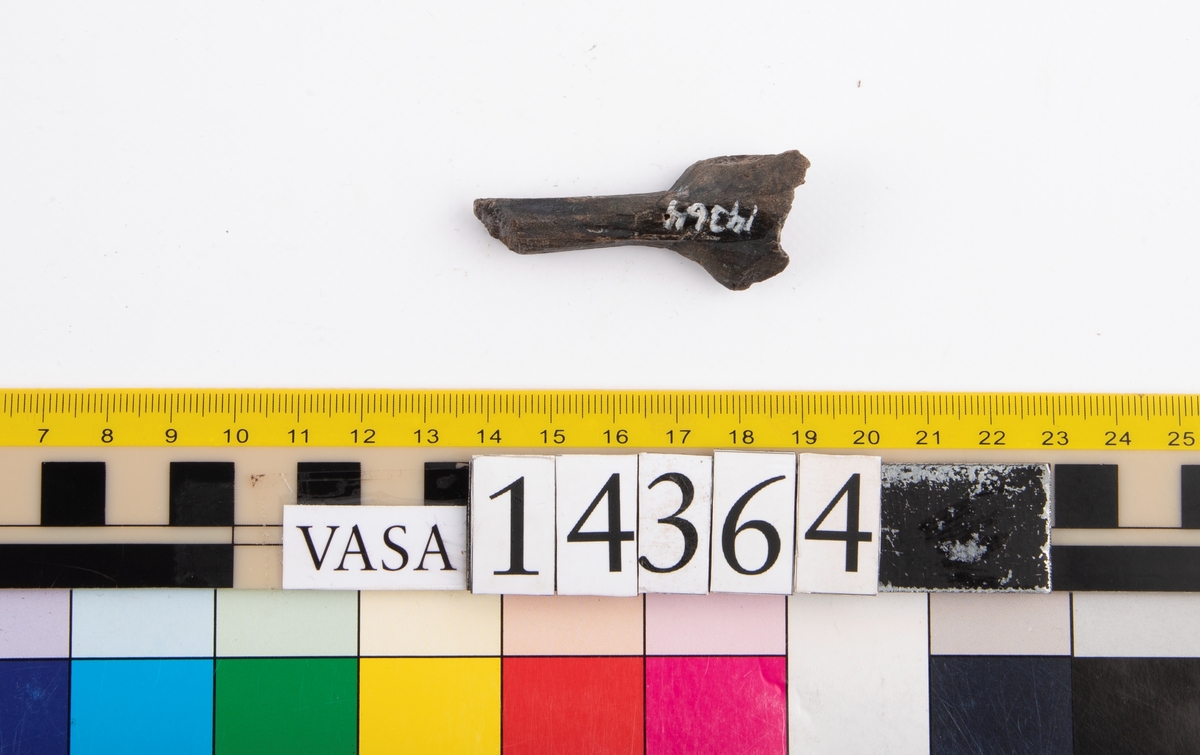 Del av en träsked. Delen utgör större delen av skedskaftet samt mindre parti av skedbladet. Skaftet är rakt och relativt smalt.

Skeddelen är bruten vid skaftänden samt upptill, vid skedbladets nedre del.

För mer information se Dokumentationsblankett under Referenser – Länkade filer.