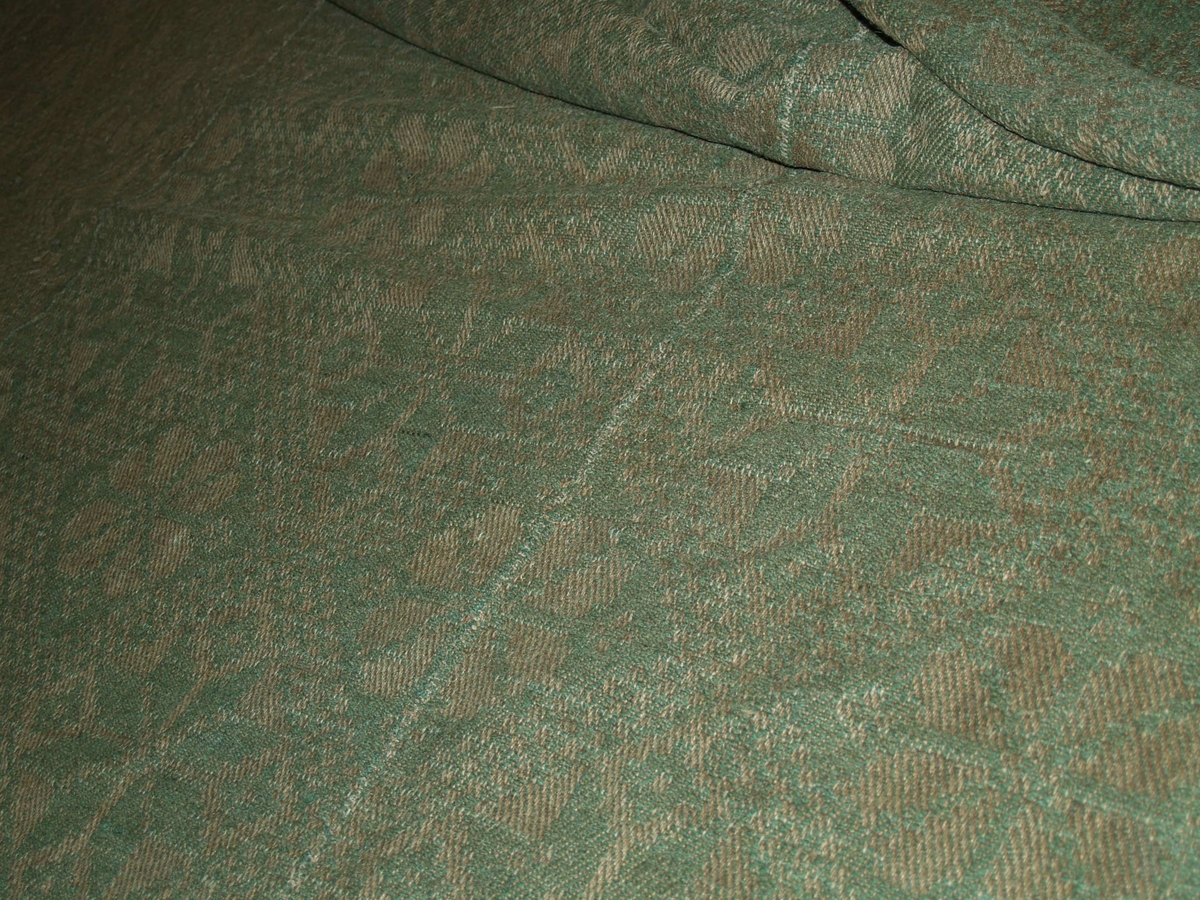 Gulvteppe i grovt stoff. Det er hånvevd og så sydd sammen. Mønster i stoffet: spisse og buede åttebladsroser. Teppet er sydd sammen av tre lengder.
I følge registreringskortet: Damaskvevning med kypert grunnbinding. Vevbredde 71 cm.