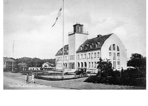Vykort, två olika versioner av samma fotografi föreställande Varbergs nya varmbadhus, som stod klart 1925. Det äldre från 1866 låg nere vid vattnet, medan detta förlades vid Strandgatan. En bil står parkerad framför badhuset. Kvarteret hette då Styrmannen men uppgår numera i kv Skepparen. (Se även bildnr F1673.)