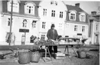 En manlig torghandlare på torget i Gränna. Flätade korgar på marken och på hans bord ligger det bland annat rotsaker.