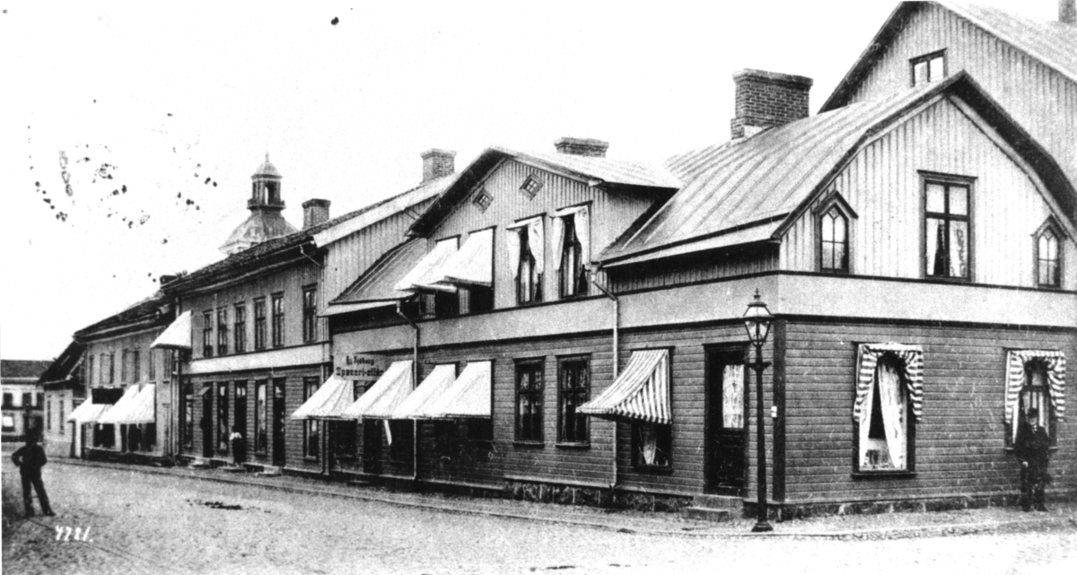 Brevkort, "Lefflerska husen vid Torg- & Östra Långgatorna, Warberg.", daterat den 18 november 1903. (Bild 2 visar även meddelandet på kortet.) Detta är kv Apotekaren utmed Torggatan. Sjöbergs speceriaffär ligger i huset närmast i bild och utmed dess gavel går Östra Långgatan. Där står en man med kubb och käpp vänd mot fotografen. Bilden är tagen mot nordväst.