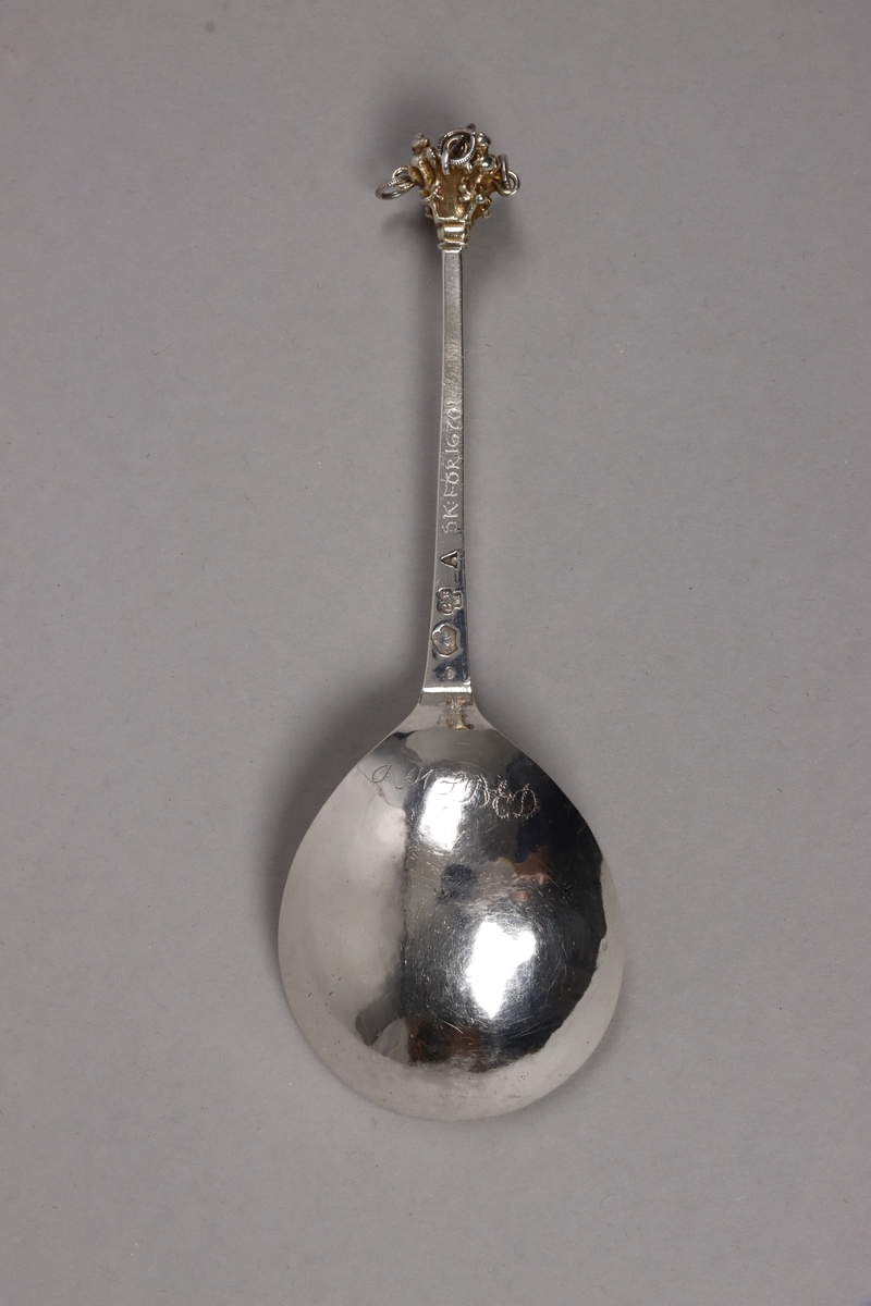 Brännvinssked av silver, med förgyllt skedblad och förgyllt dekorelement på handtaget. Skeden är utsågad ur plåt och har sedan fått drivet och graverat skedblad samt slagen ytdekor på handtaget. I änden sitter ett gjutet dekorelement med fem fastlödda ringar, i vilka sitter varsin större silverring och skramlar lite. Graverat på skedbladets undersida: NNS BED (delvis svårtytt). Stämplat på handtagets undersida: (svårtytt) stadsstämpel -  bockhuvud, CBM, A.