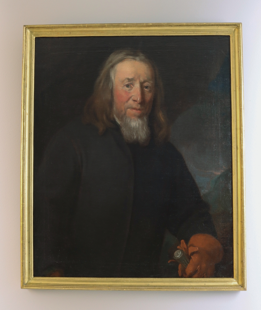 Porträtt av Erik Ersson. Midjestycke åt höger. Ersson med gråsprängt hår, svart tillknäppt rock och brun handske på vänsterhand, vilken greppar den andra handsken samt en käpp. Käppen med silverknapp varpå "E.E.S" står skrivet. 