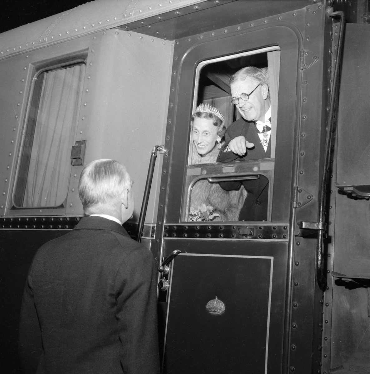 Linköpings central 1953. Landshövding Carl Hamilton vinkar av kung Gustaf VI Adolf och drottning Louise efter deras besök av Linköping i samband med parets Eriksgata. Besöket hade avslutats med middag på Linköpings slott, vilket förklarar galaklädseln. Kungen har en egen tågvagn vars dörrar pryds med den kungliga kronan.