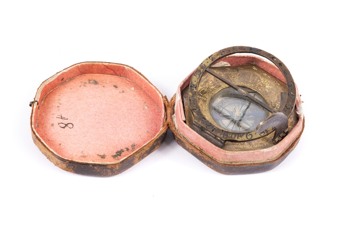 Solur med kompass, rosen orienterad för ca 10 grader västlig missvisning. Båge för polhöjd försilvrad. Etui 8-kantigt, svart läder.