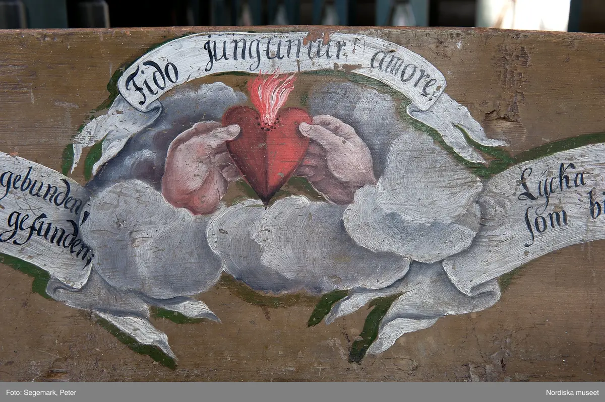Brudstol (vigselstol) med plats för två i Julita kyrka, Södermanland. På ryggens framsida det brinnande hjärtat, en kärlekssymbol och text på tyska, latin och svenska.. Brudstolen har troligen ursprungligen stått i Arbrå kyrka, Hälsingland. Datering 1770-1780-tal.