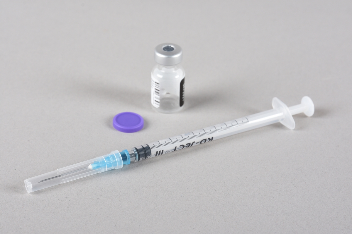 Vaksinasjonsutstyr brukt ved første vaksine mot Covid-19, satt i Bergen 05.01.2021. Utstyret består av en engangssprøyte med kanyle og beskyttelseshette og et åpnet hetteglass for Pfizer-vaksine, med tilhørende kork.