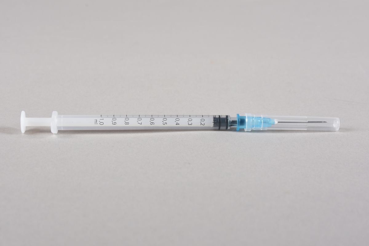 Vaksinasjonsutstyr brukt ved første vaksine mot Covid-19, satt i Bergen 05.01.2021. Utstyret består av en engangssprøyte med kanyle og beskyttelseshette og et åpnet hetteglass for Pfizer-vaksine, med tilhørende kork.