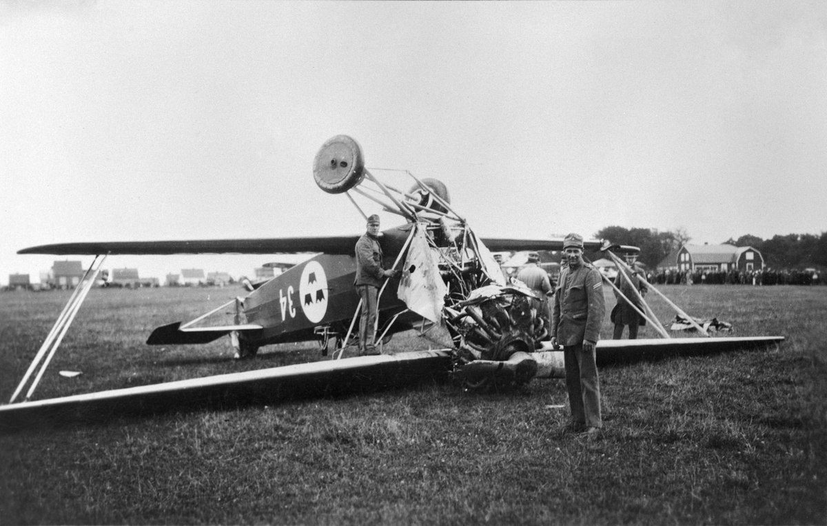 Flygplan S 6, Fokker C.VE nr 34 har landat upp och ned, omkring 1930. Militärer kring flyglanet, folksamling i bakgrunden.