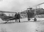 Flygplan Albatros SW 20, nr 752, står framför motorverkstaden och B-hangaren vid Flygkompaniets verkstäder på Malmen, vintertid omkring 1920-1922. Tre mekaniker vid flygplanet.