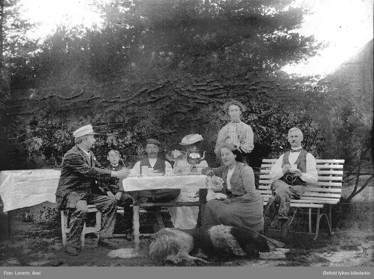 Gruppeportrett av ukjente, som drikker kaffe i hagen. KAn det være fotografens familie?