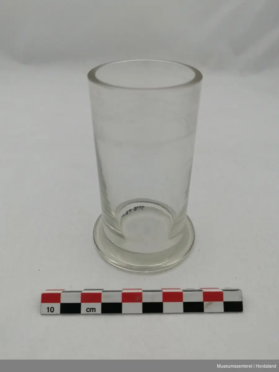 Form: sylinderforma med flat, rund botn, vidare enn sjølve glaset
