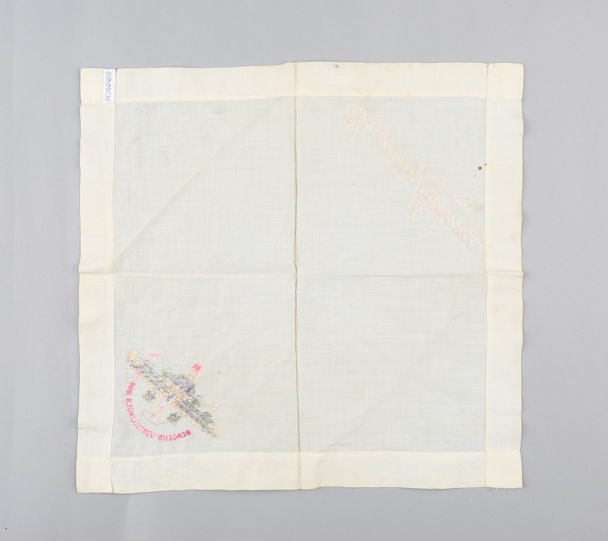 Tekstilserviett med brodert motiv av hovedpaviljongen på Bergensutstillingen i 1898. Også brodert et navn. Servietten er faldet med maskinsøm