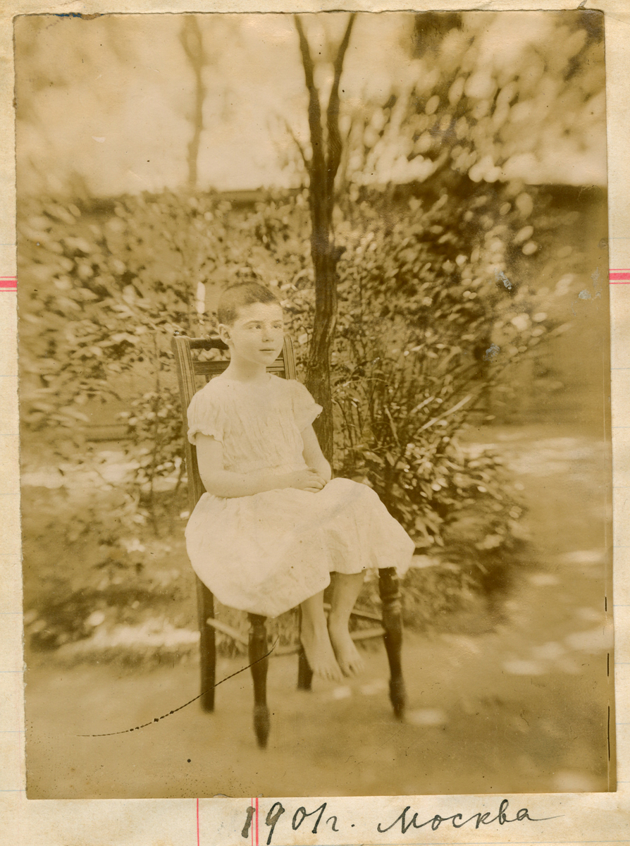 Portrett av et barn, antagelig Victoria Rostin kortklippet, sittende på en stol. Fotografert utendørs.