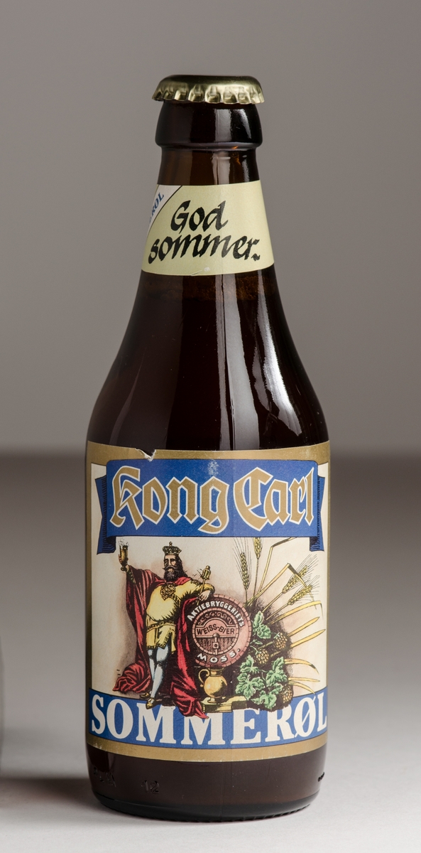 Ølflaske i brunt glass med gullfarget crown cork og pålimt etikett foran og bak. Liten etikett på halsen.