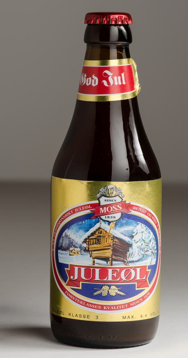 Ølflaske i brunt glass med etikett foran, bak og på hals. Rød crown cork med datostempel.