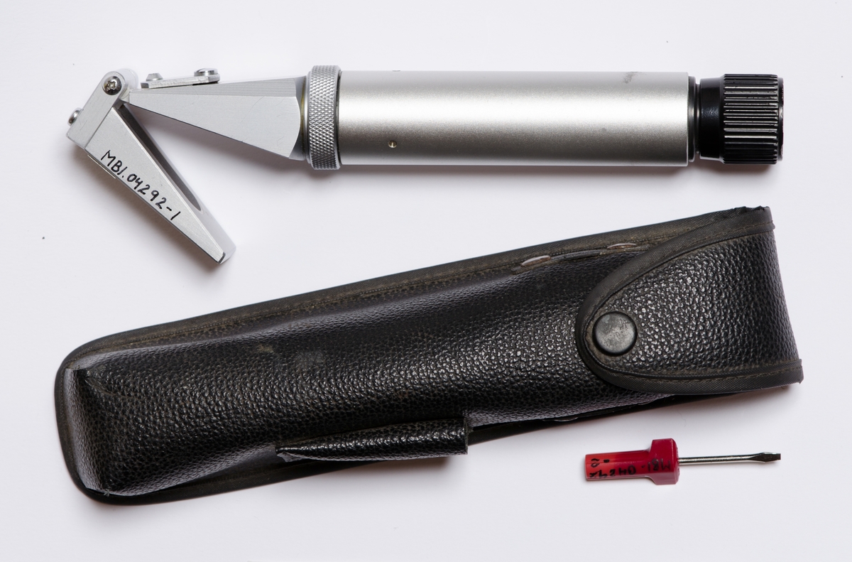 Sylinderformet instrument med to påfestede deler formet som pyramider i enden. Sort etui med kneppelukning i enden med trykknapp. Liten lomme på siden til skrujern. Skrujern med rødt skaft.