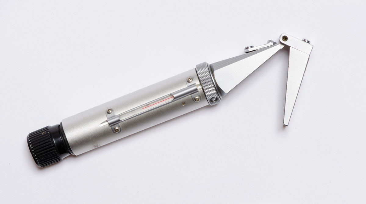 Sylinderformet instrument med to påfestede deler formet som pyramider i enden. Sort etui med kneppelukning i enden med trykknapp. Liten lomme på siden til skrujern. Skrujern med rødt skaft.